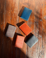 Five leather wallets in different colors on a wooden surface